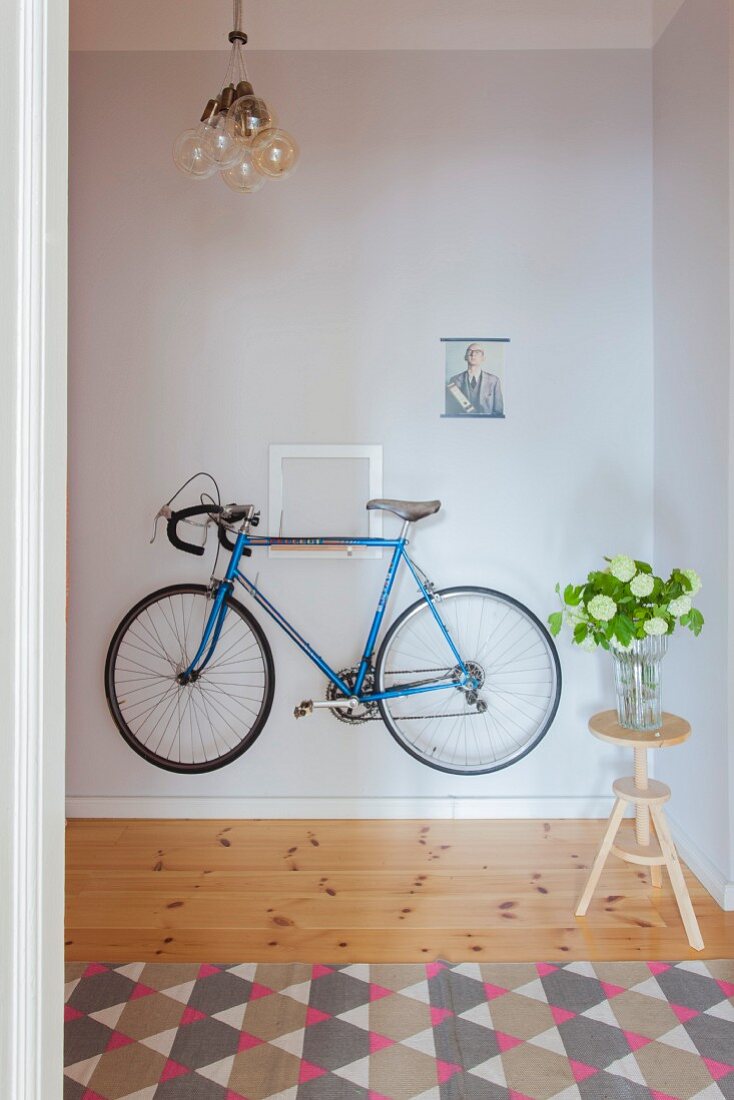 Blue bike hung on hallway wall next to flowers on stool