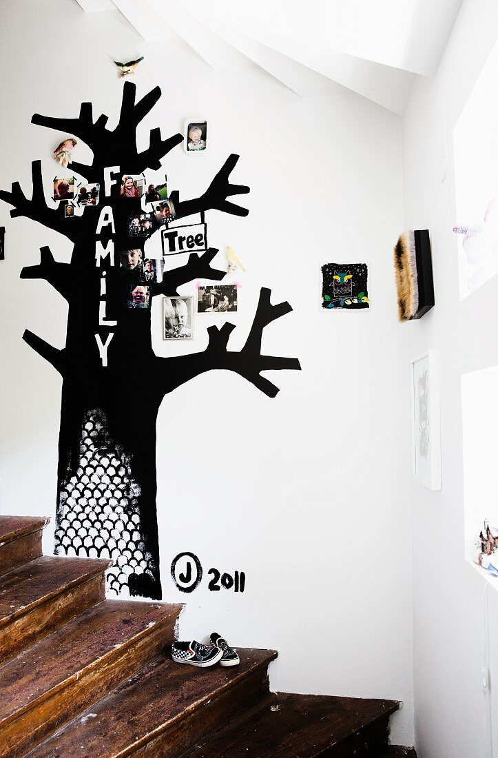 Rustikale Holztreppe und schwarzer Stammbaum mit Familienfotos an weisser Wand