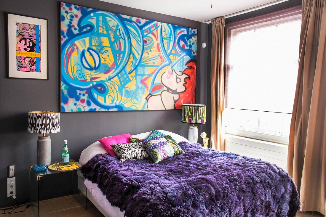 Buntes Bild mit Graffito über Bett mit violetter Felldecke