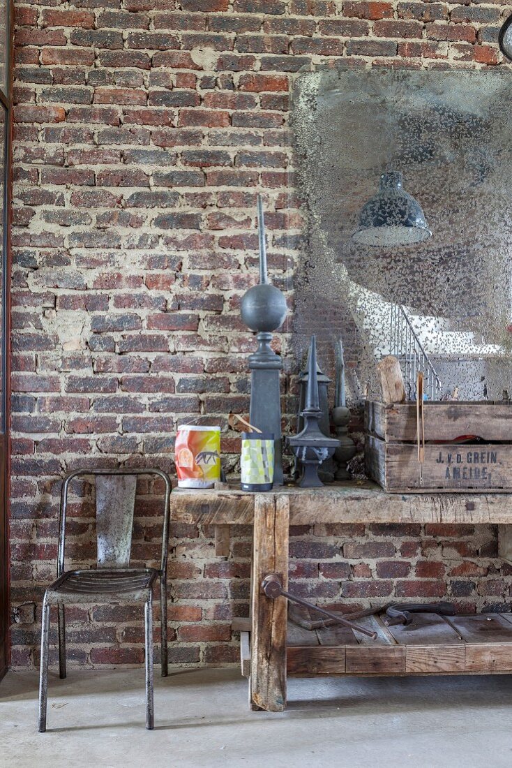 Old workbench and metal chair below patinated mirror on brick wall