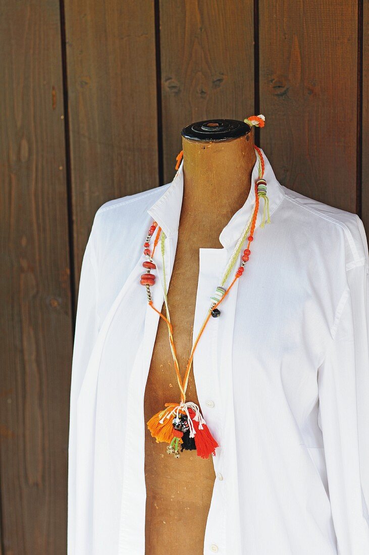 Necklace made from various crocheted cords, wooden beads and tassels hanging on tailors' dummy wearing white blouse