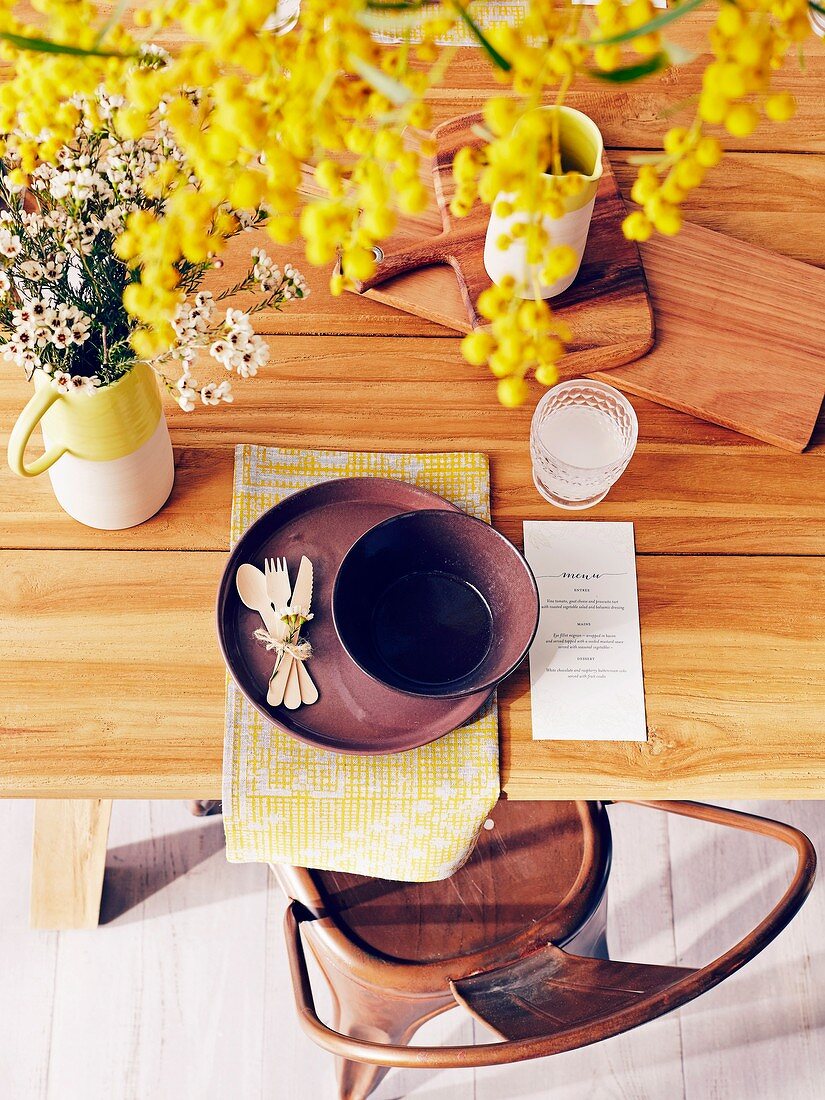 Gedeck mit Holzbesteck und gelbem Tischset, Wachskrautstrauß und gelbem Blütenzweig