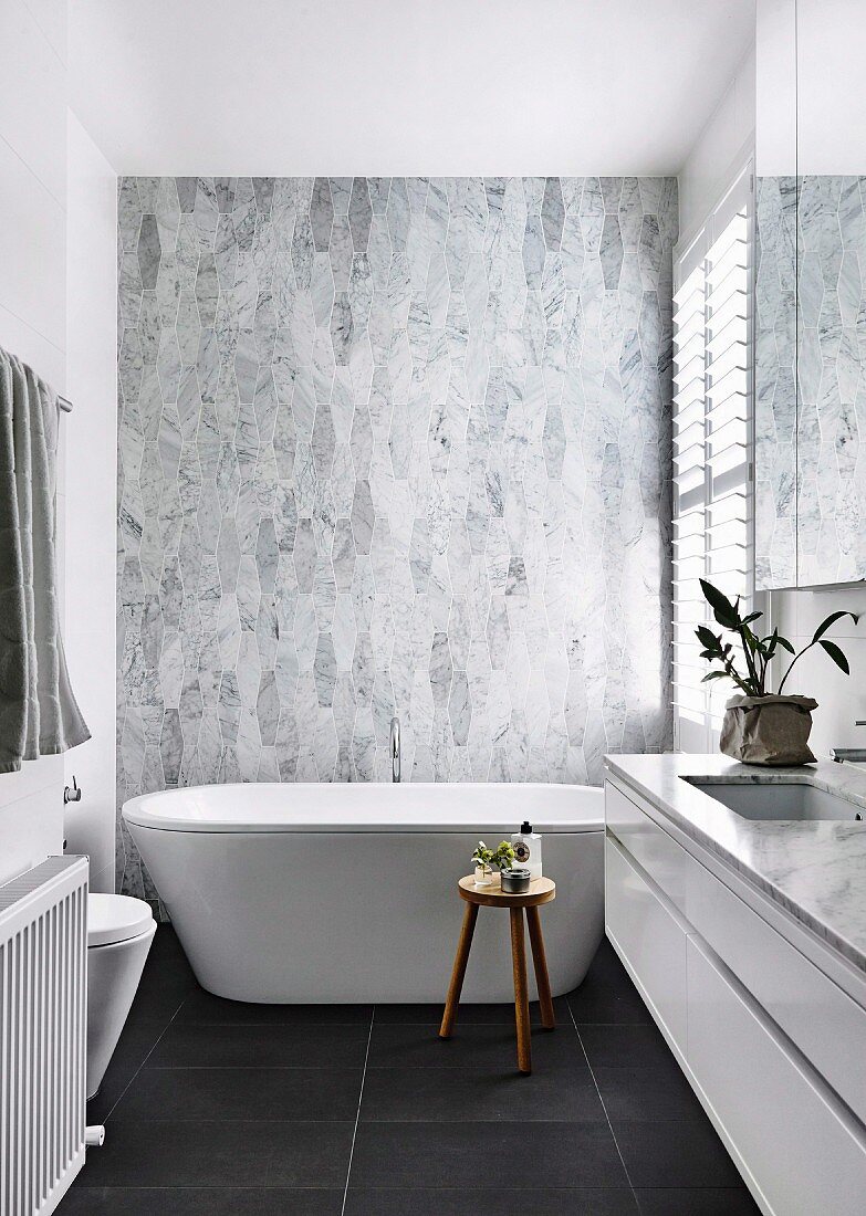 Designer bathroom with free-standing bathtub in front of marble tiles and black floor tiles