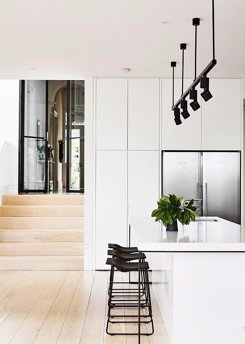 weiße Kücheninsel und Barhocker unter Lichtschiene mit schwarzen Strahlern in offener Küche