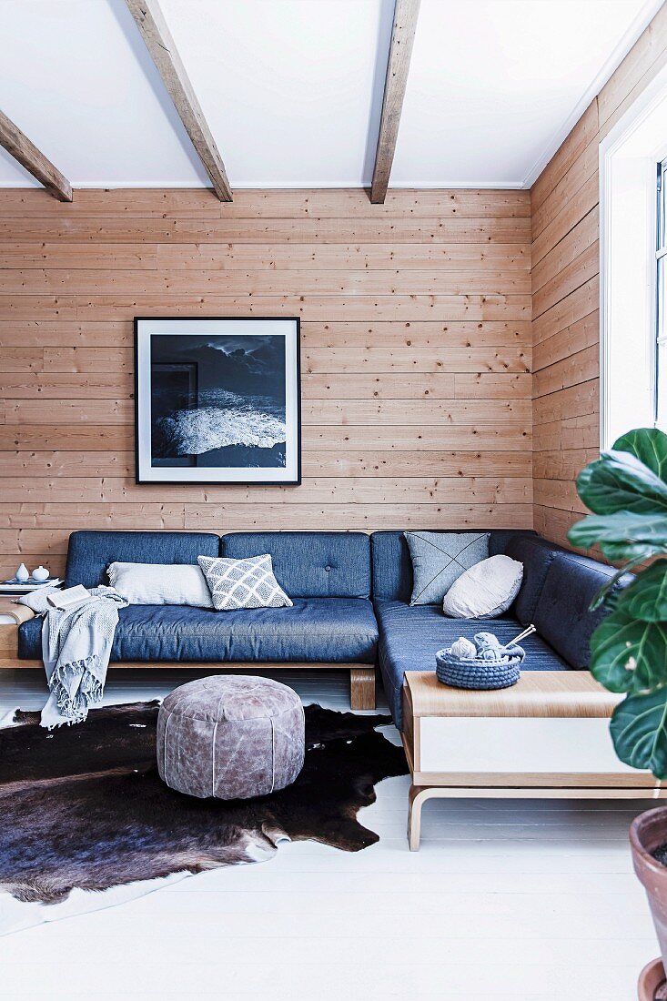 Ecksofa mit blauen Polstern vor rustikaler Holzwand in Wohnzimmerecke