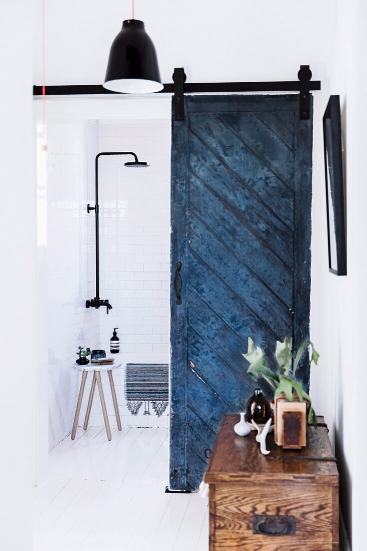 Bathroom with blue vintage door leaf as sliding element and rain shower