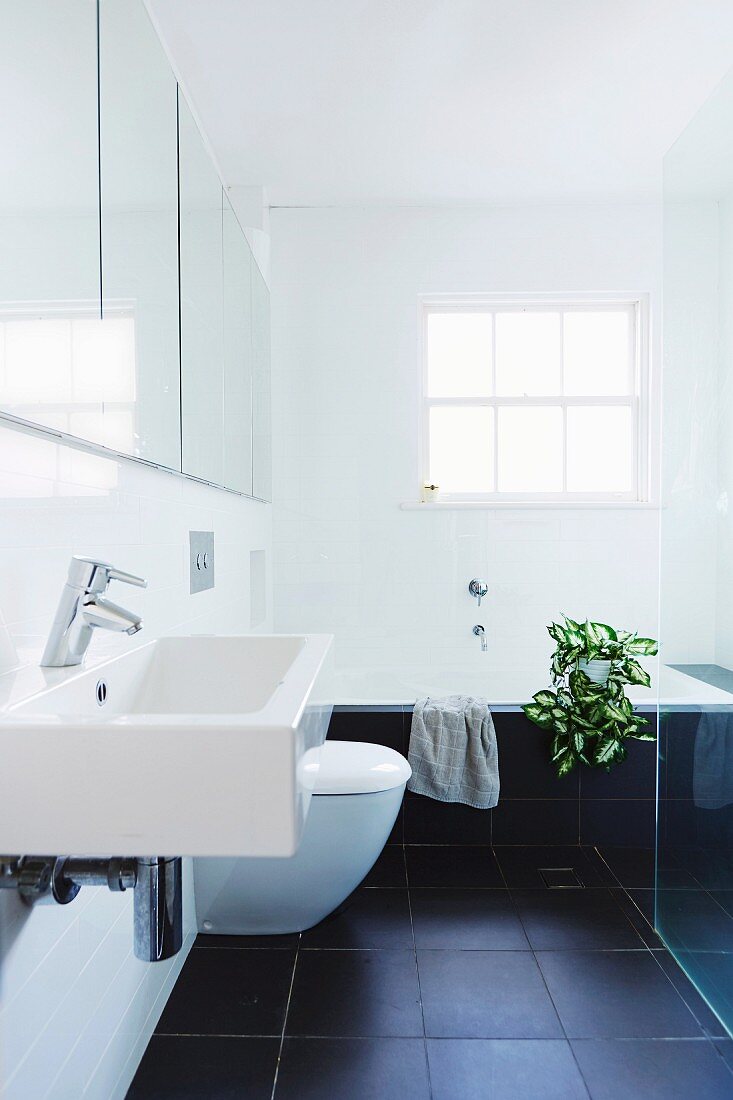 Modern bathroom with black tiled floor, white sink in front of a mirror cabinet