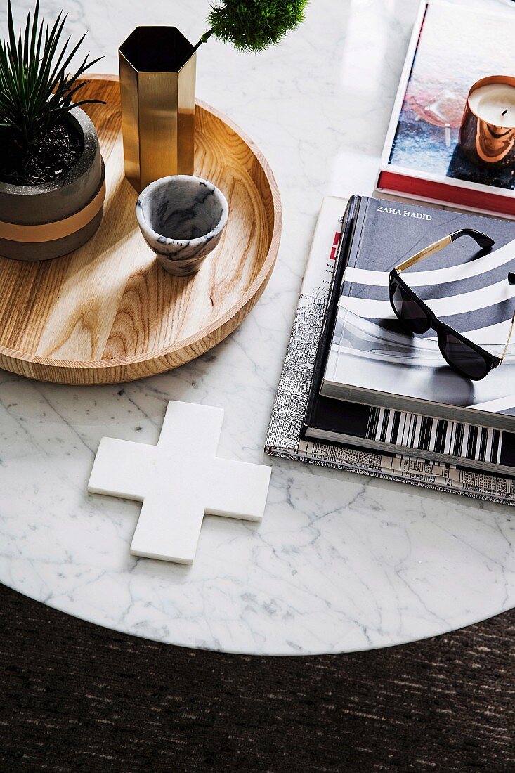 Pile of books with sunglasses and wooden tray with green plant on round marble table