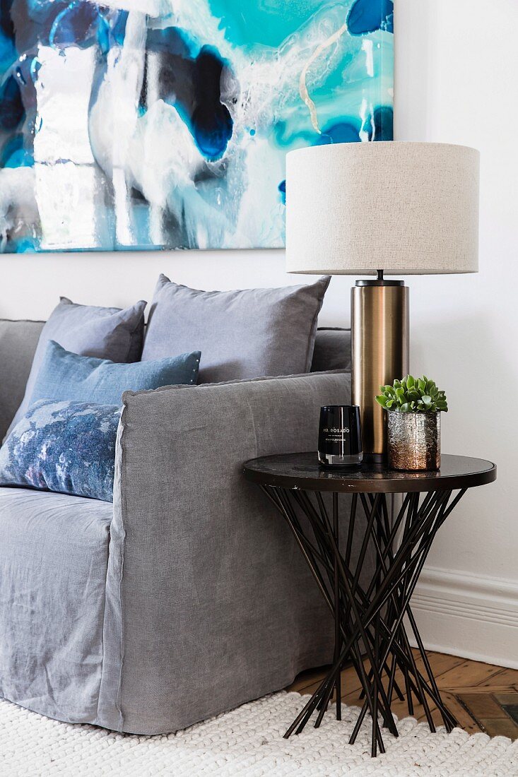 Elegant table lamp on side table next to gray couch, modern picture on wall