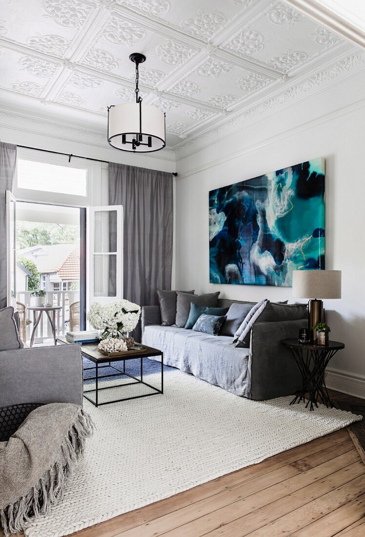 Graue Couchgarnitur vor modernem Bild im Wohnraum mit Stuckdecke