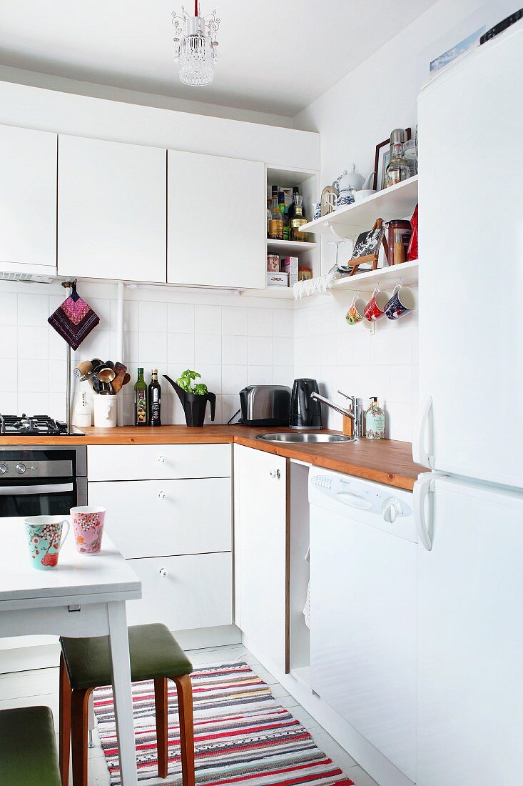 Corner of white kitchen with wooden worksurface, bracket shelves and wall cabinets