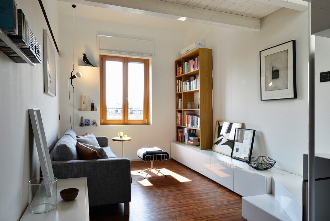 Wohnraum mit grauer Couch, weißem Lowboard und Bücherregal