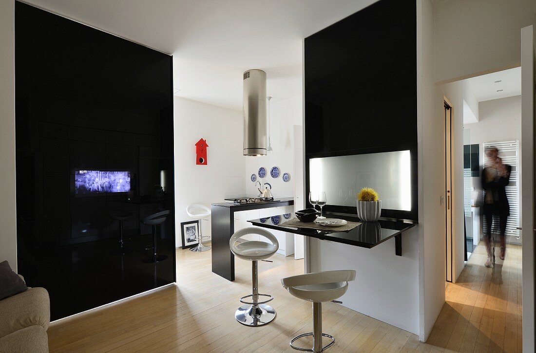Schwarze Wandscheibe mit integriertem Bildschirm und Raumteilerwand mit klappbarer Hochglanz-Tischplatte