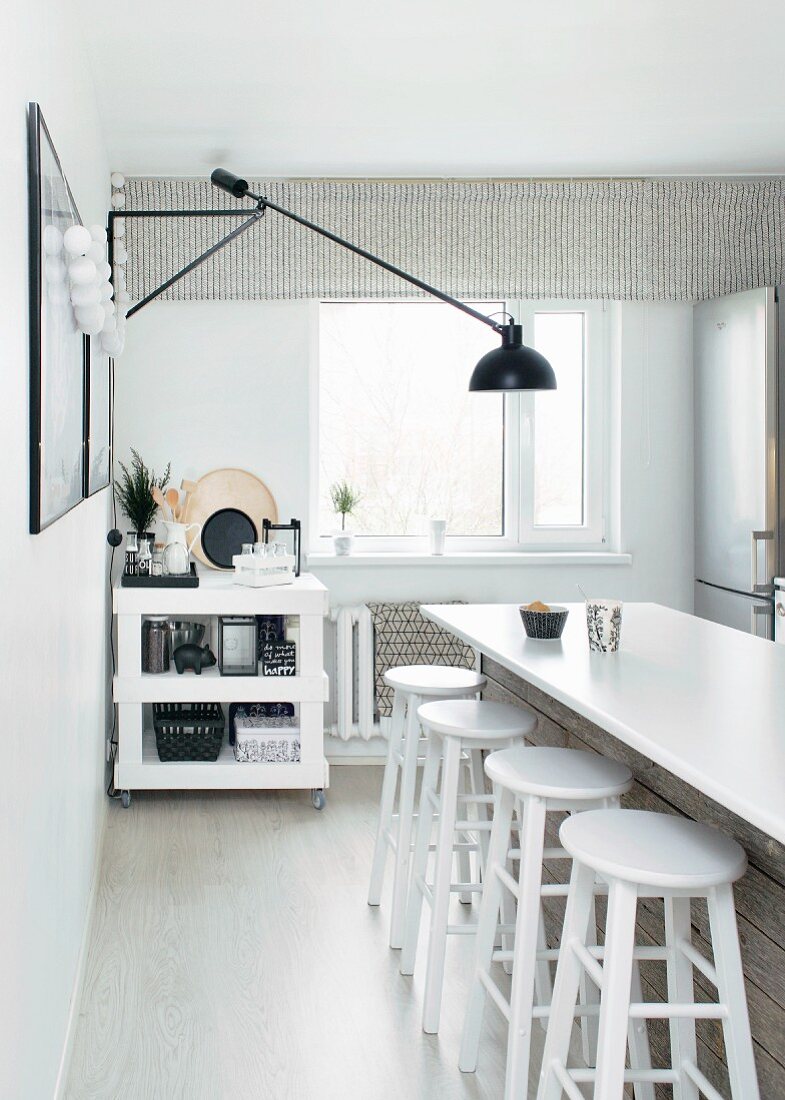 weiße Küchentheke mit Barhockern, an Wand schwarze Wandleuchte mit Kragarm