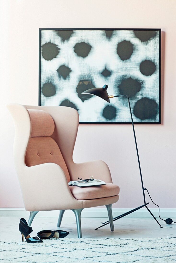 Pink wing chair and black floor lamp in front of a modern picture on a pink wall