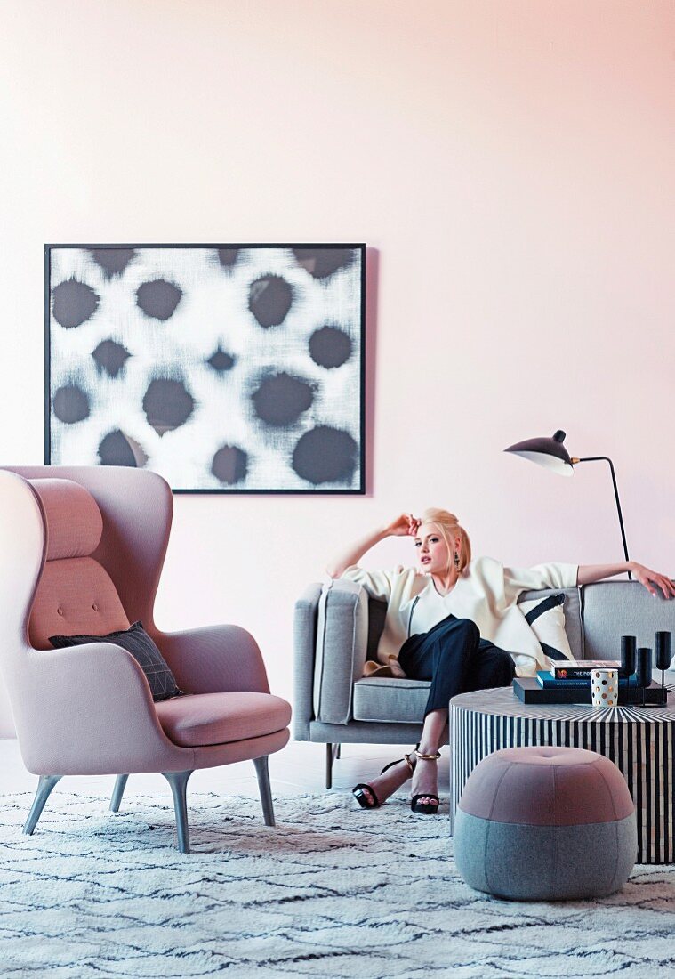 Woman on gray sofa next to pink wing chair and pouf