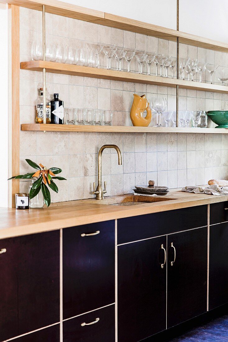 Küchenzeile mit schwarzen Fronten und Regalbrettern an Wand mit Gläsern