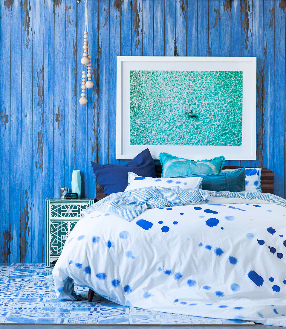 Doppelbett mit gemusterter Bettwäsche vor blauer Stellwand
