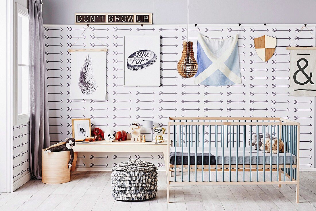 Kinderzimmer mit Gitterbett und Sitzpouf, Konsolentisch mit Spielzeug vor Mustertapete mit Pfeilmotiven