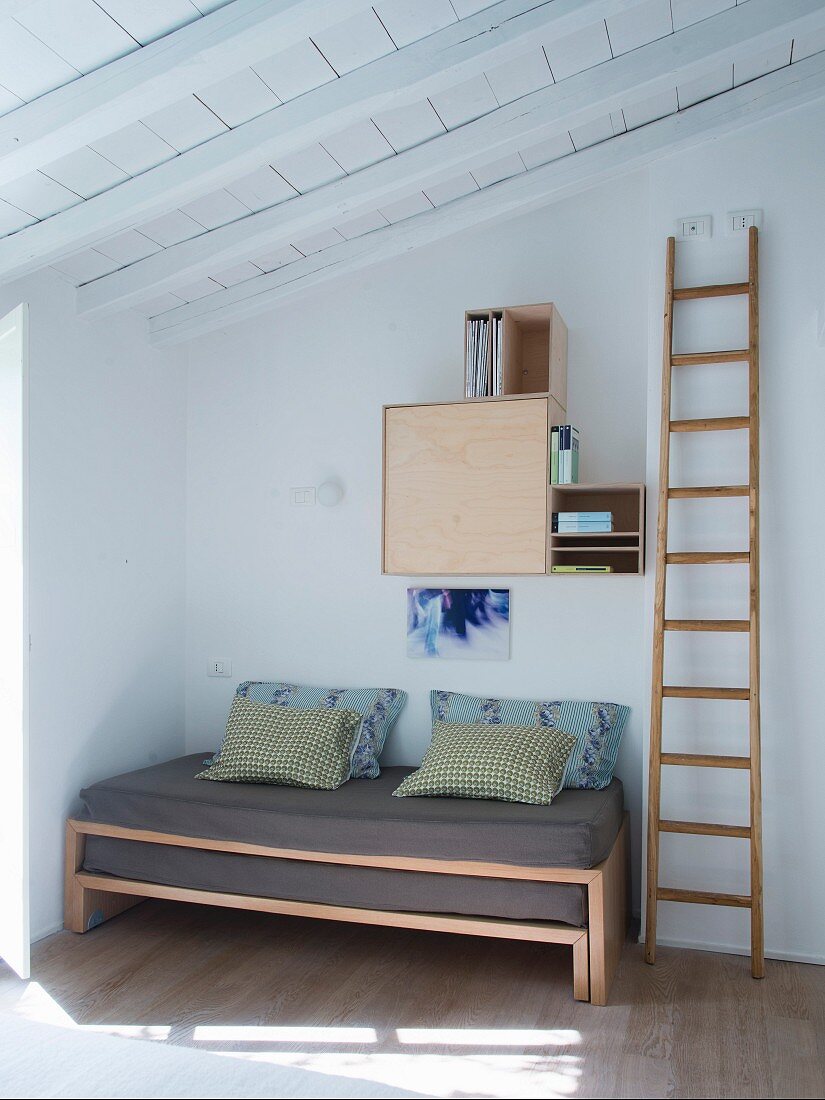 Holzleiter neben ausziehbarem Bett in Zimmerecke, an Wand aufgehängte Regalmodule