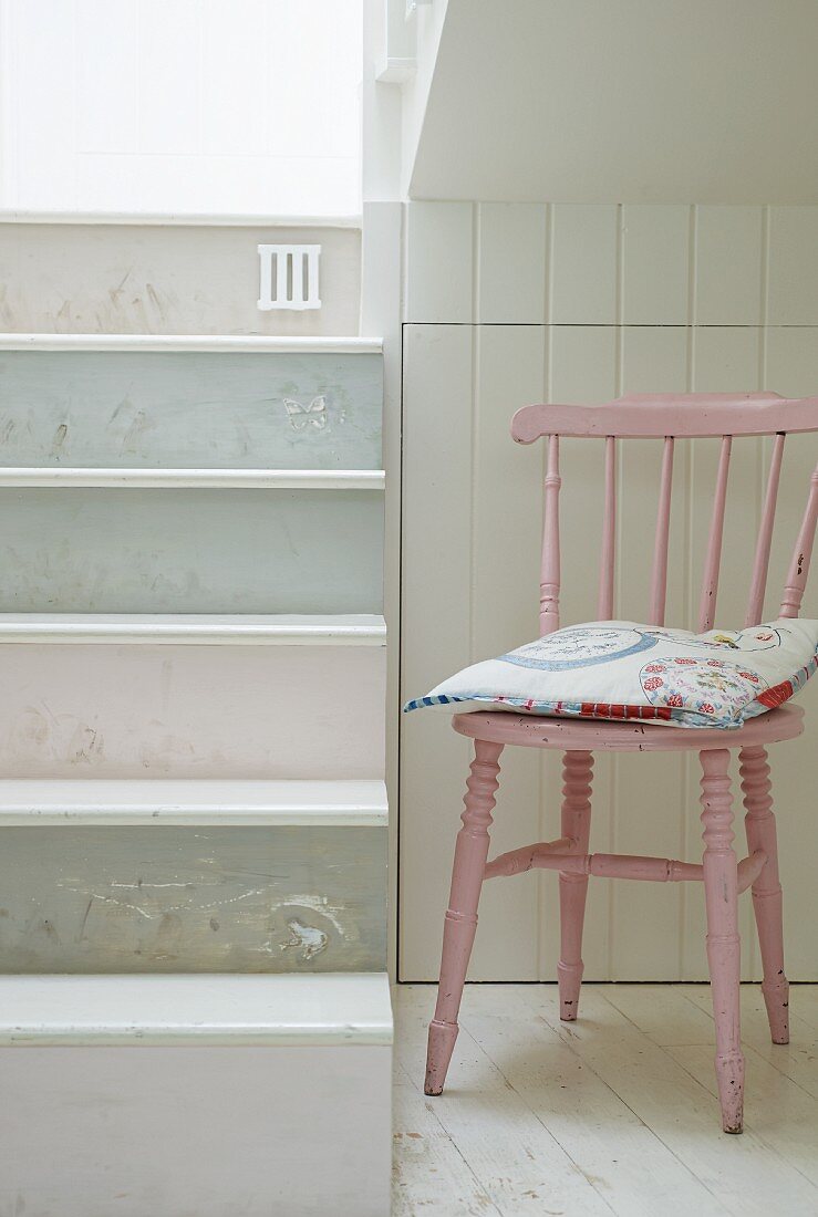 Rosa lackierter Küchenstuhl in Treppennische, seitlich Stufen pastellfarben lackiert