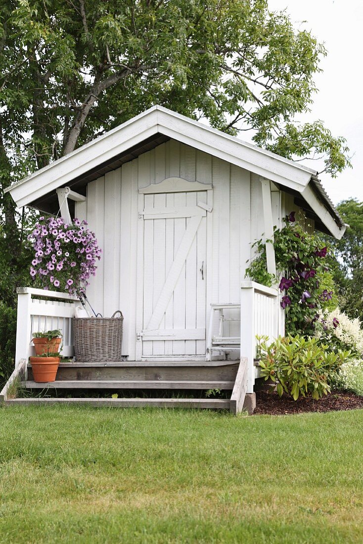 Weisses Gartenhäuschen aus Holz mit kleiner Veranda und Blumenampel