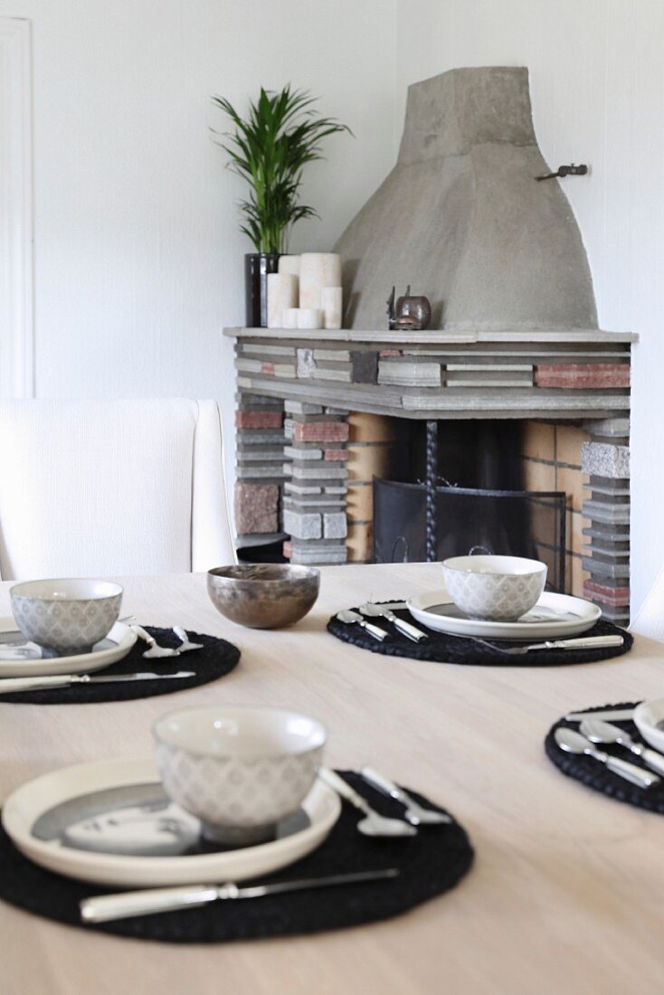 Place settings with black place mats on wooden table in front of brick fireplace