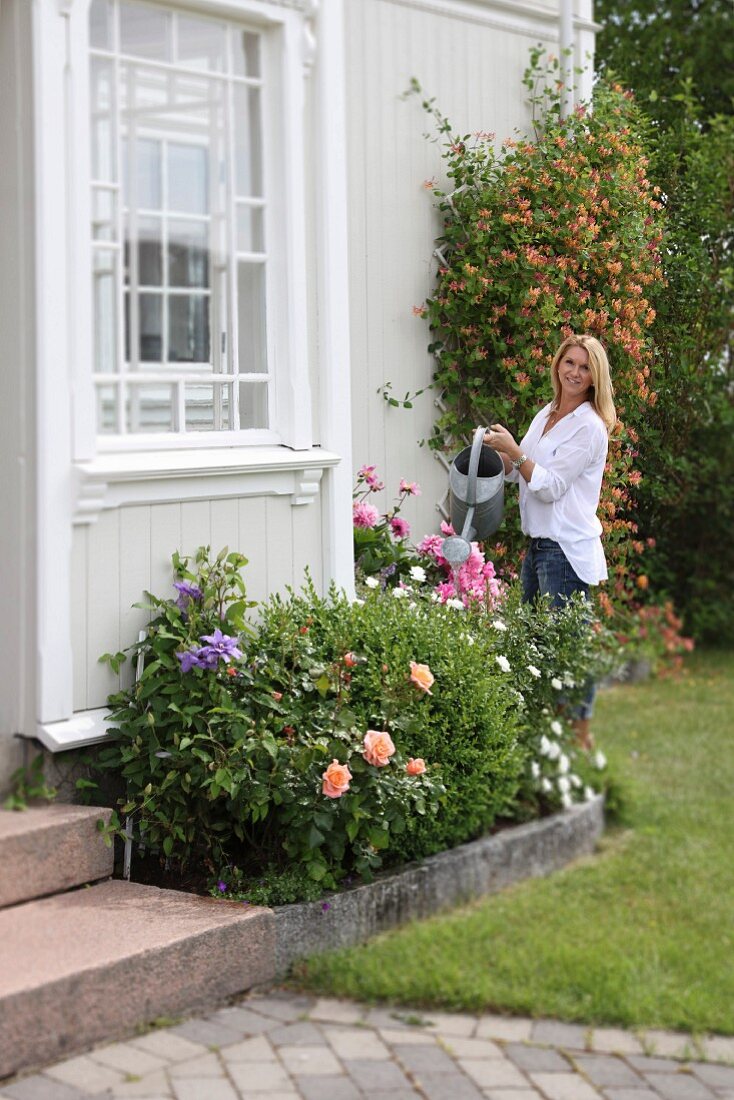 Woman watering flowers outside traditional country house