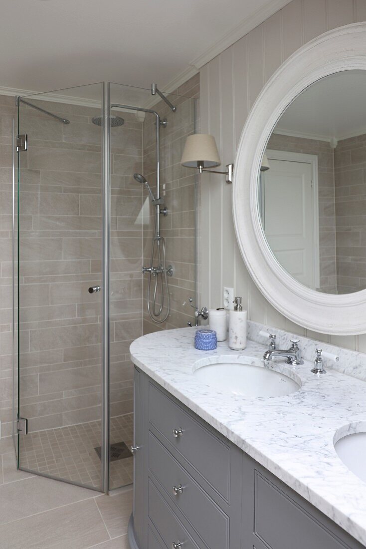 Massgefertigter Waschtisch mit Marmorplatte und zwei Waschbecken vor rundem Wandspiegel und barrierrefreiem Duschbereich