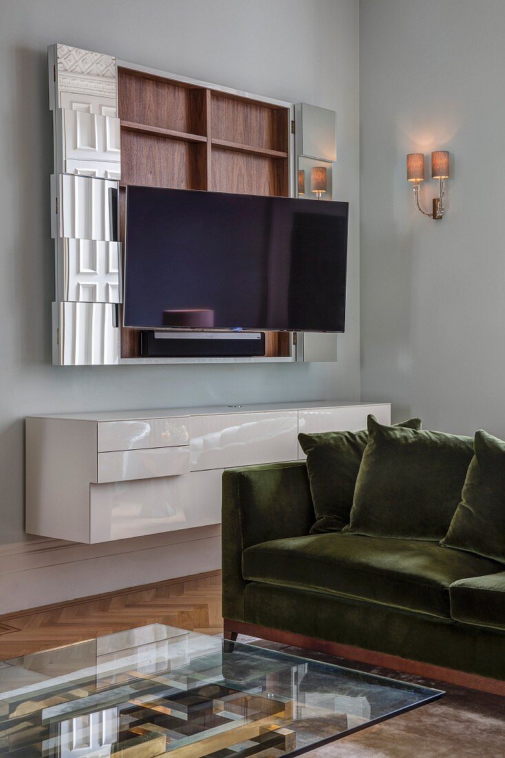 Wohnraumecke mit Glas-Couchtisch vor Sofa, an Wand offener TV-Hängeschrank über weißem Hängesideboard