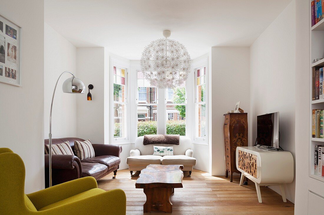 Eklektizistisch möblierter Wohnraum mit Erker, kugelförmige Pendelleuchte über Holz-Couchtisch, im Hintergrund antike Sofas