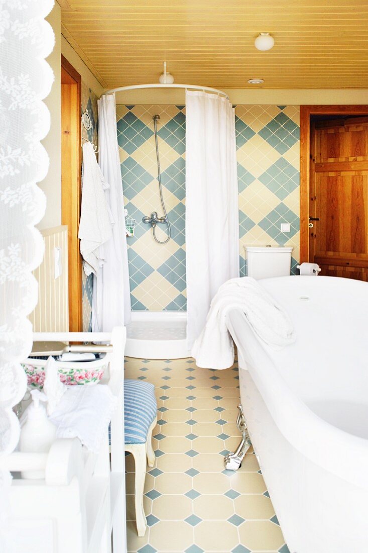 Freistehende weiße Badewanne und Dusche in blau-beige gefliestem Bad