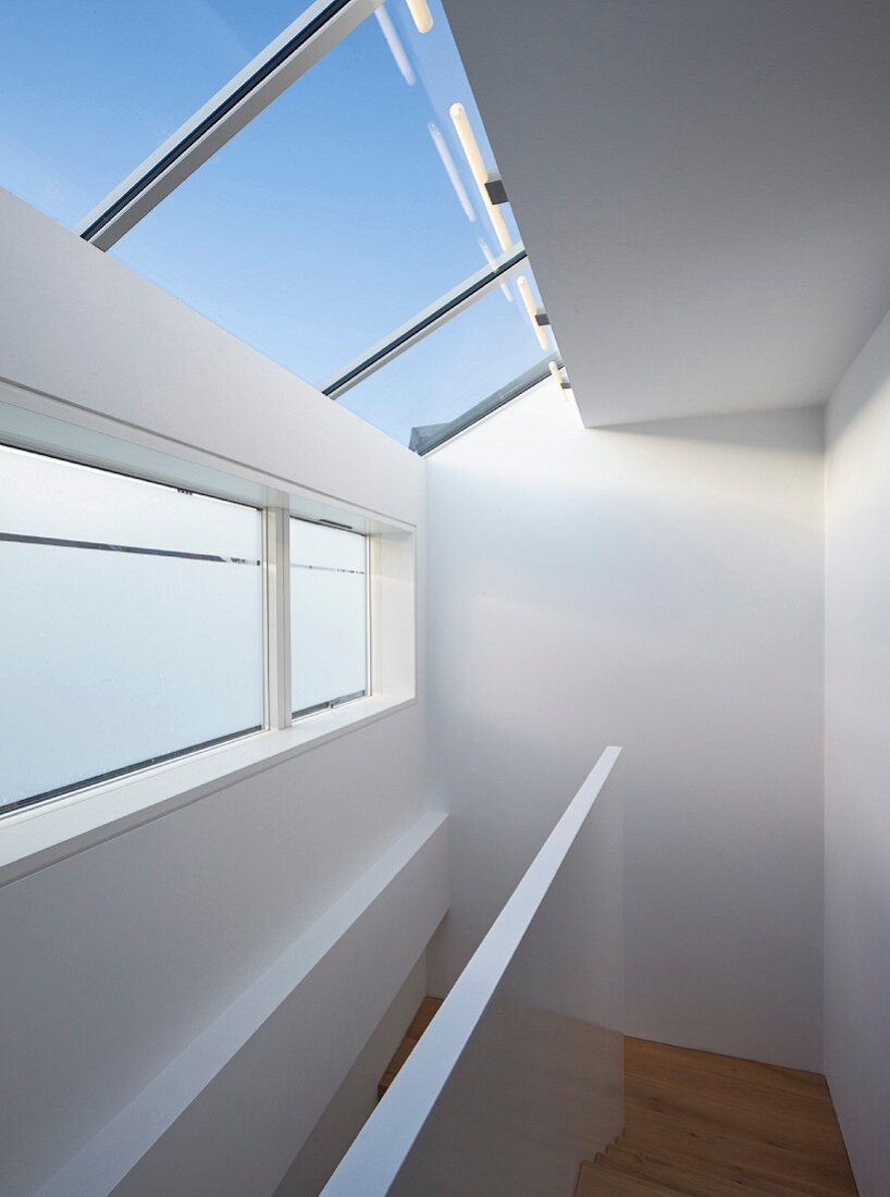 Moderner Treppenraum mit weißer Brüstungsmauer, Oberlichtern und Dachfenstern