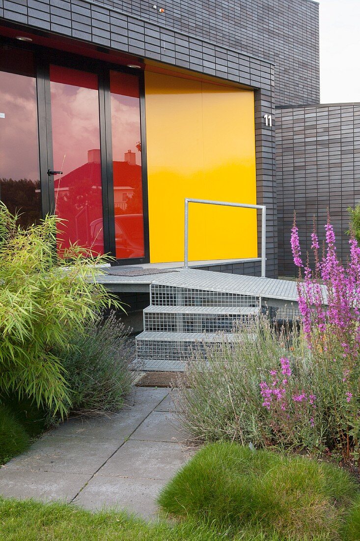 Metal steps and ramp leading into modern house with red glass terrace doors and yellow wall panel