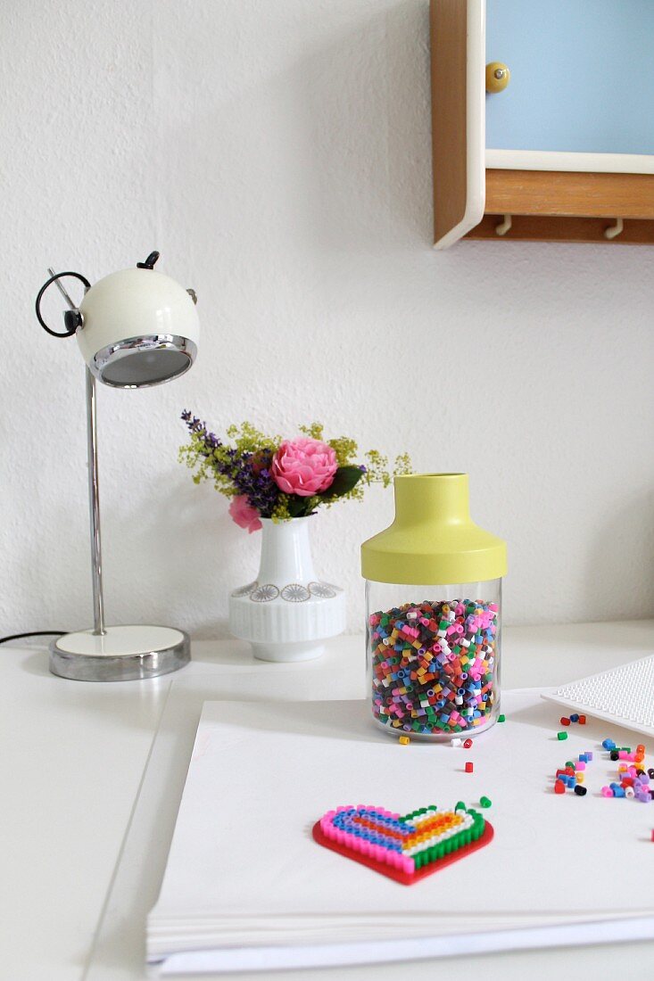 Bunte Bügelperlen und Blumensträusschen in Retro Vase auf weißem Schreibtisch