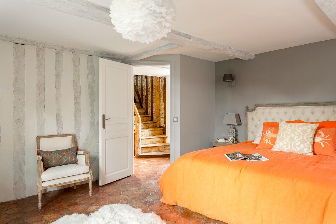 Doppelbett mit orangefarbener Bettwäsche in restauriertem Schlafzimmer mit Blick auf rustikale Holztreppe