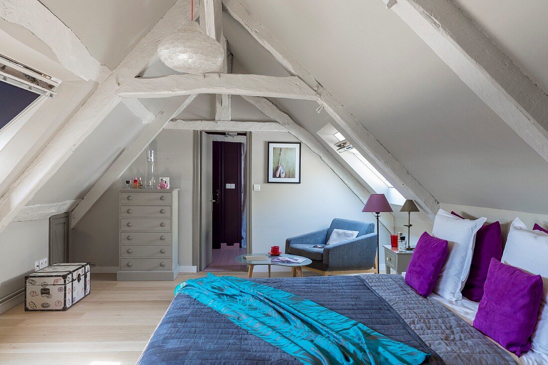 Schlafzimmer unter dem Dach mit Holzbalken und bunter Bettwäsche
