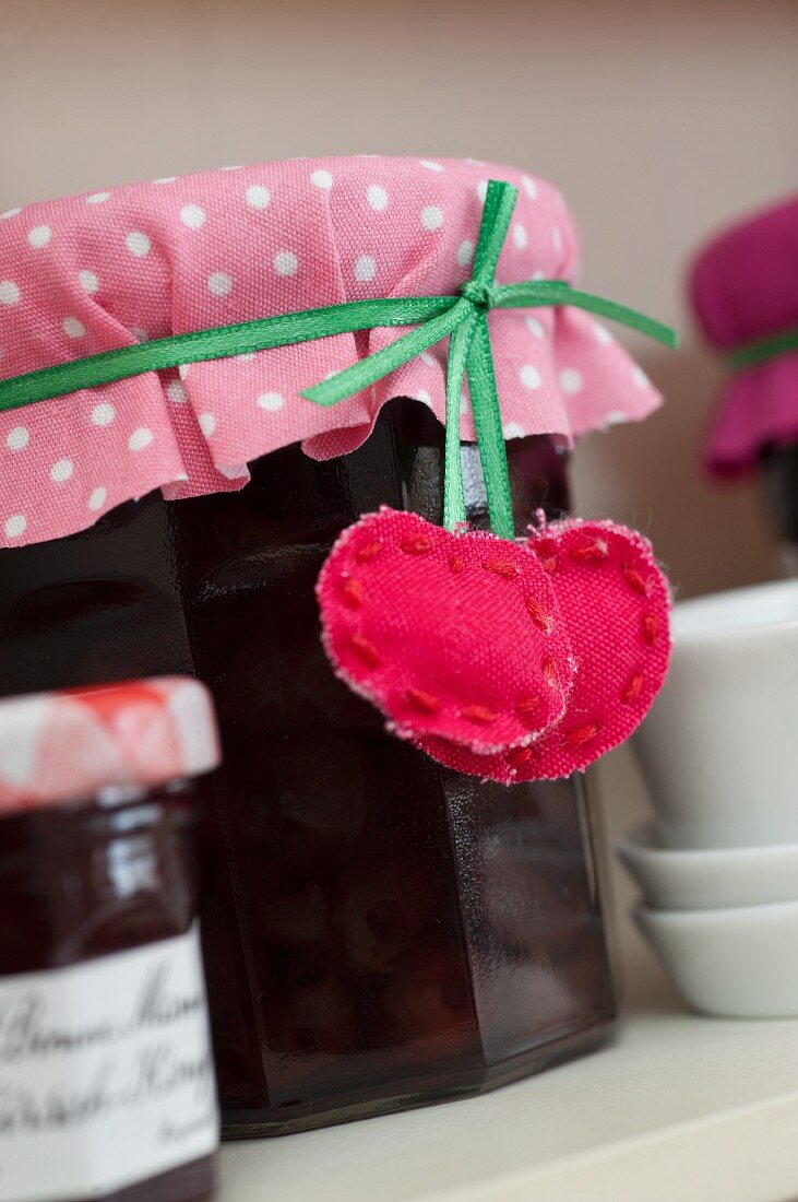 Marmeladenglas mit rosa-weiss gepunktetem Stoff und DIY-Kirschanhänger verziert