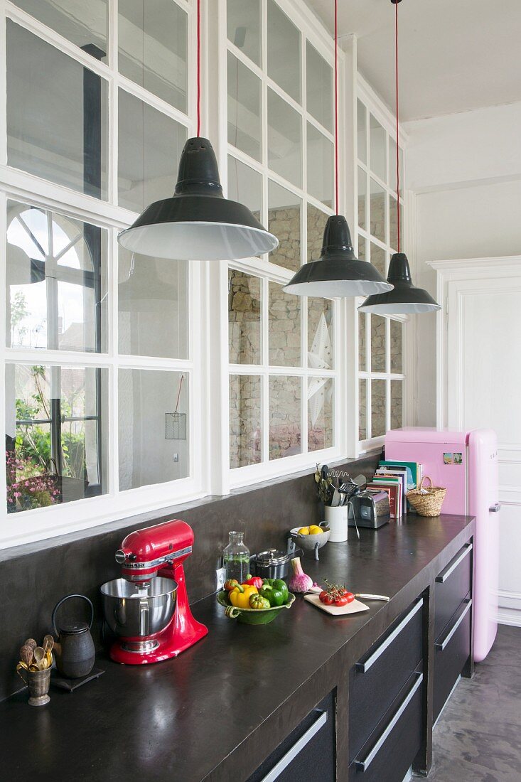 Black kitchen counter and pink fridge below interior windows in loft apartment