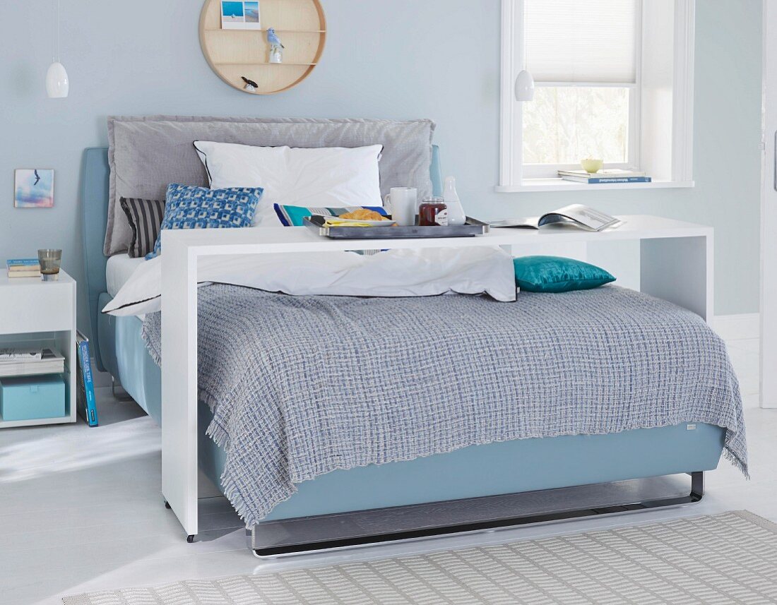 A boxspring bed with a bed bridge in a bedroom in blue shades