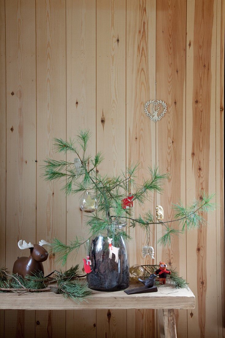 Festively decorated pine branches in glass jar of bark on rustic bench