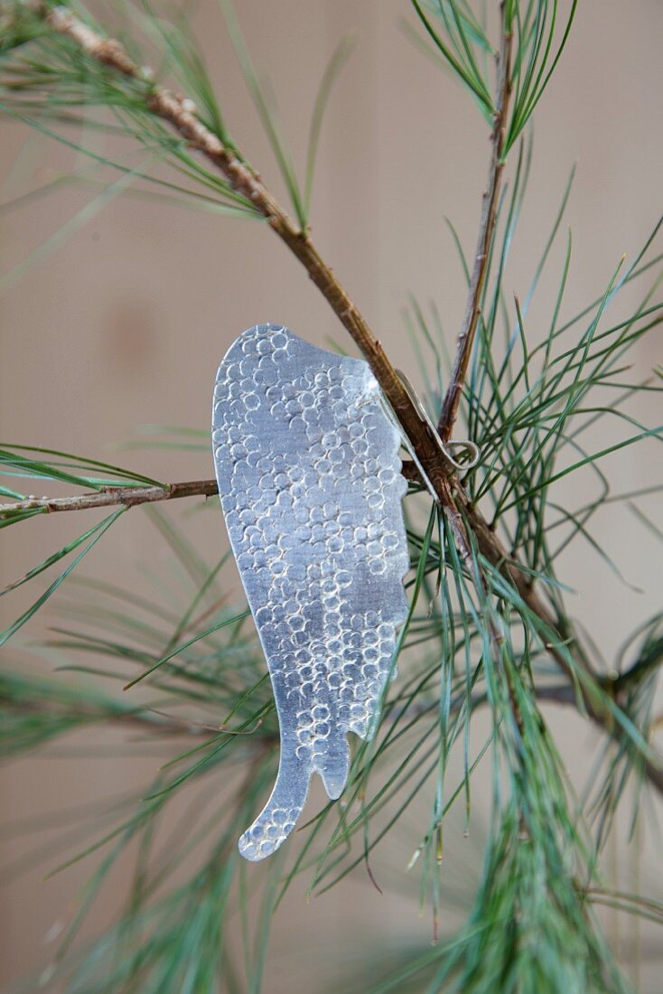 Metal angel wing hung from pine branch