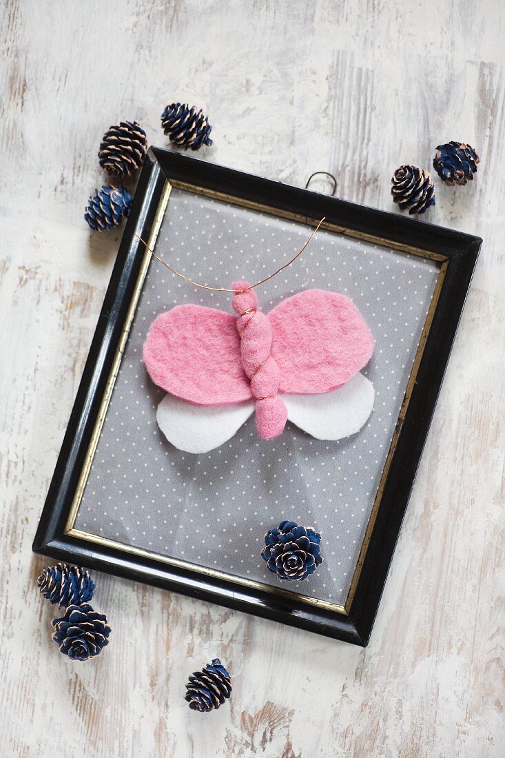 DIY-Schmetterling aus Filz in Vintage Bilderrahmen, umgeben von Kieferzapfen