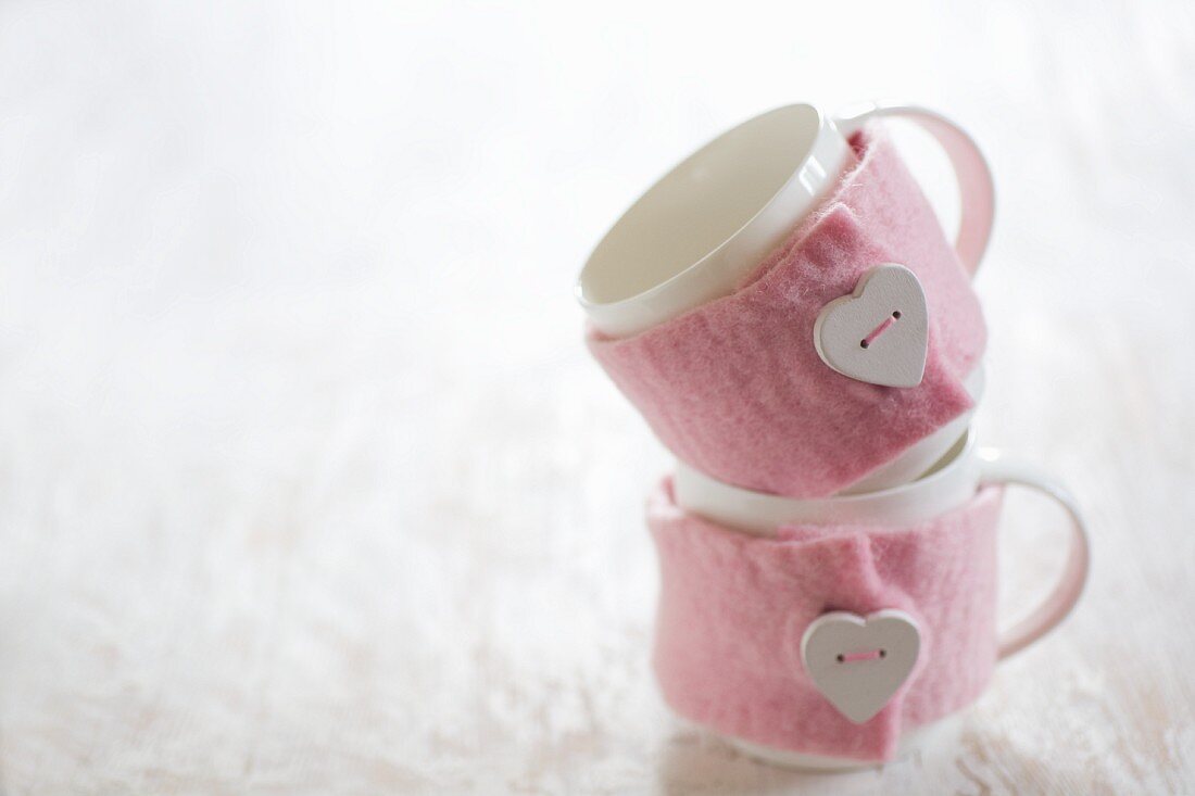 Tassen mit rosafarbenen DIY-Filzwärmern und aufgenähten herzförmigen Knöpfen