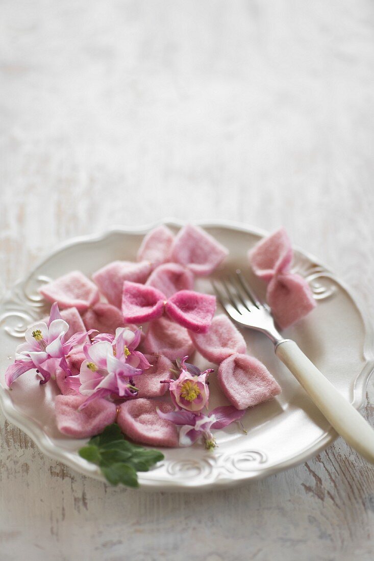 DIY-Schleifen aus rosa Filz und rosa Blüten auf weißem Teller mit Gabel