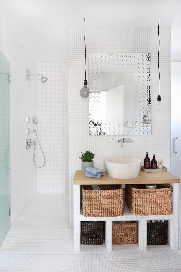 Tiled washstand with storage baskets and countertop sink and view into accessible shower area