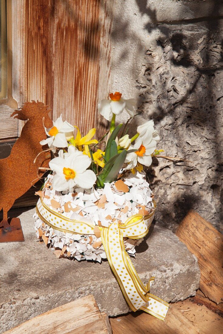 Narcissus and forsythia in vase covered in pieces of egg shell