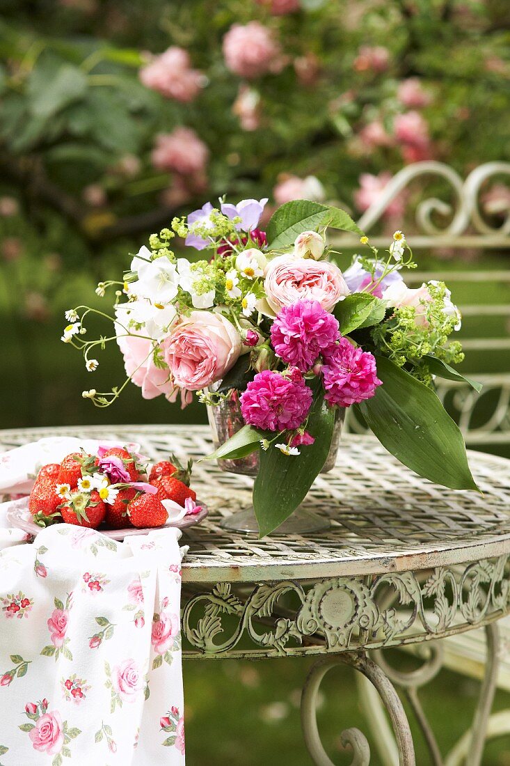 Romantischer Blumenstrauss und frische Erdbeeren auf Vintage Metalltisch im Garten