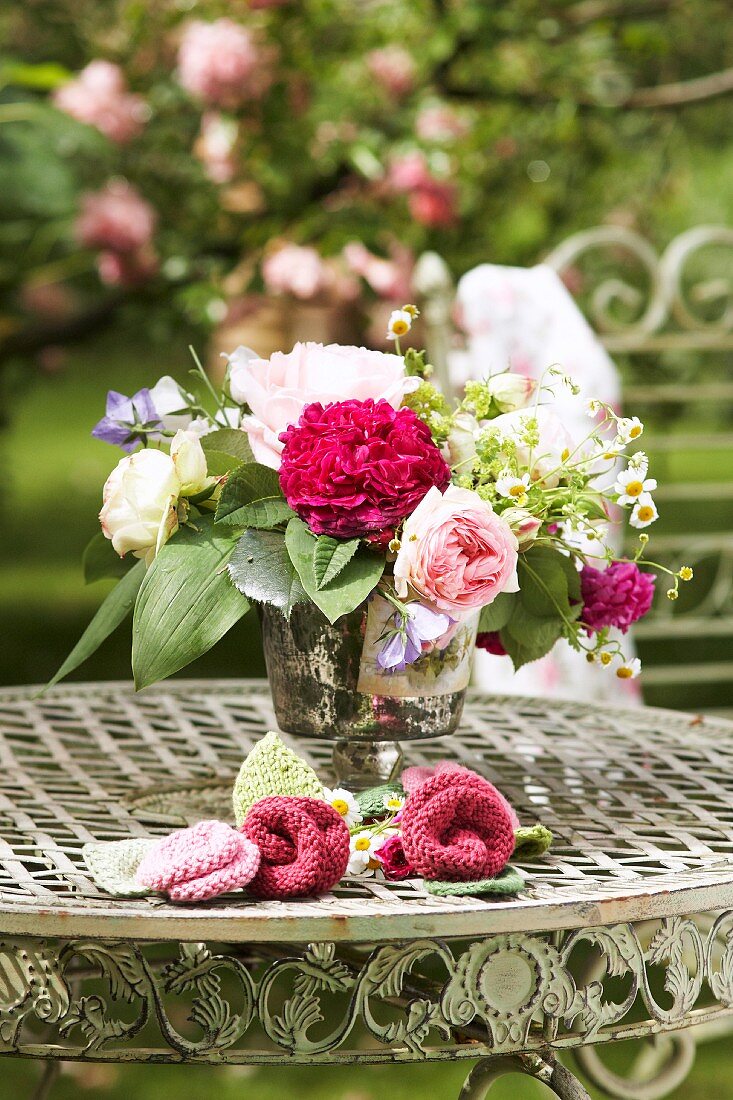 Romantischer Blumenstrauss und Strickblüten auf rundem Vintage Metalltisch im Garten