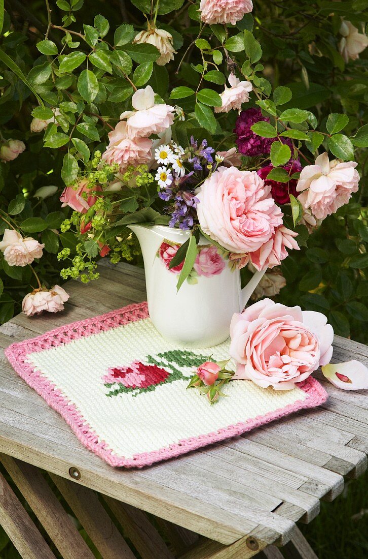 Romantic vase of garden flowers on knitted cloth with rose motif